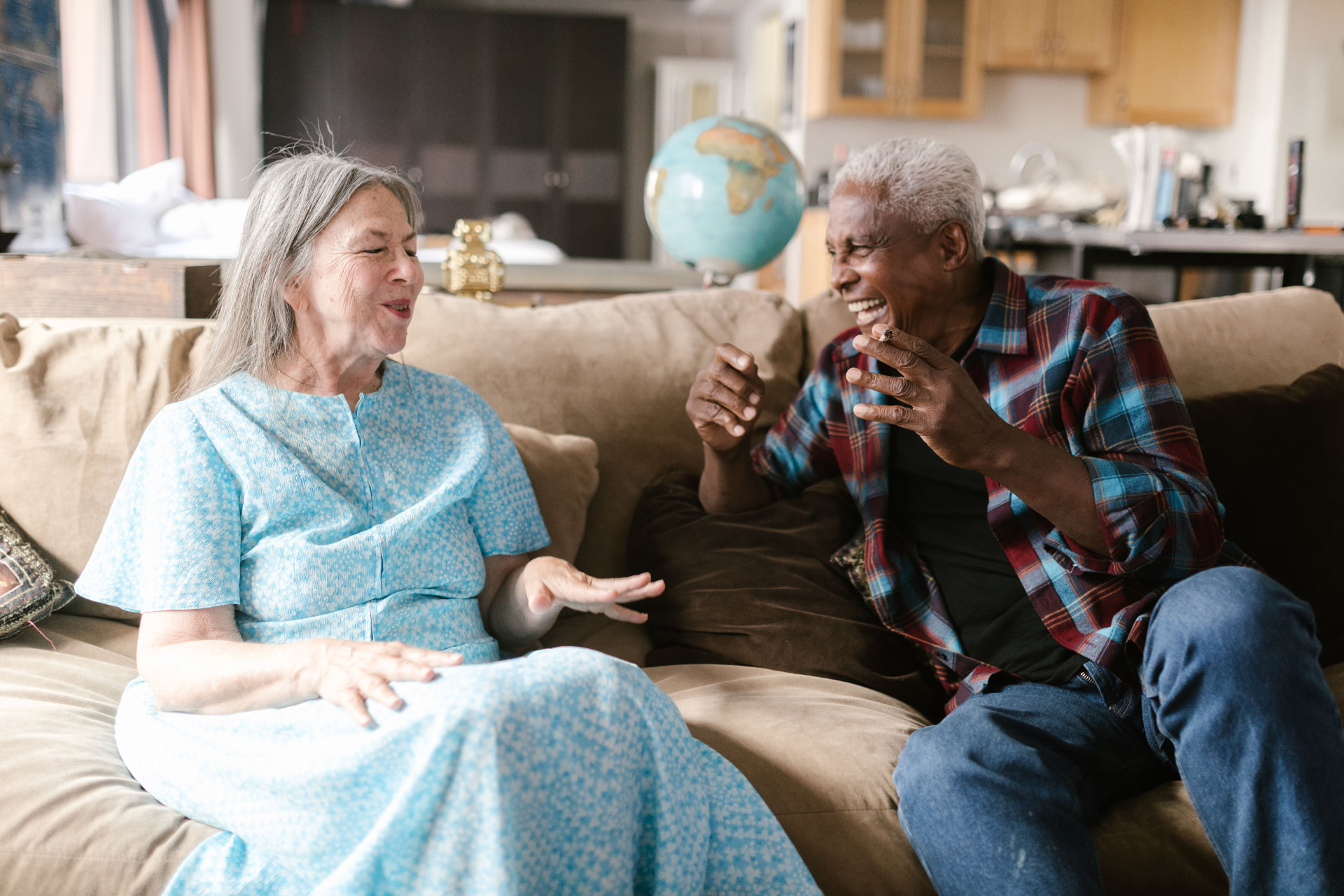 Two older adults laughing together on a couch at home