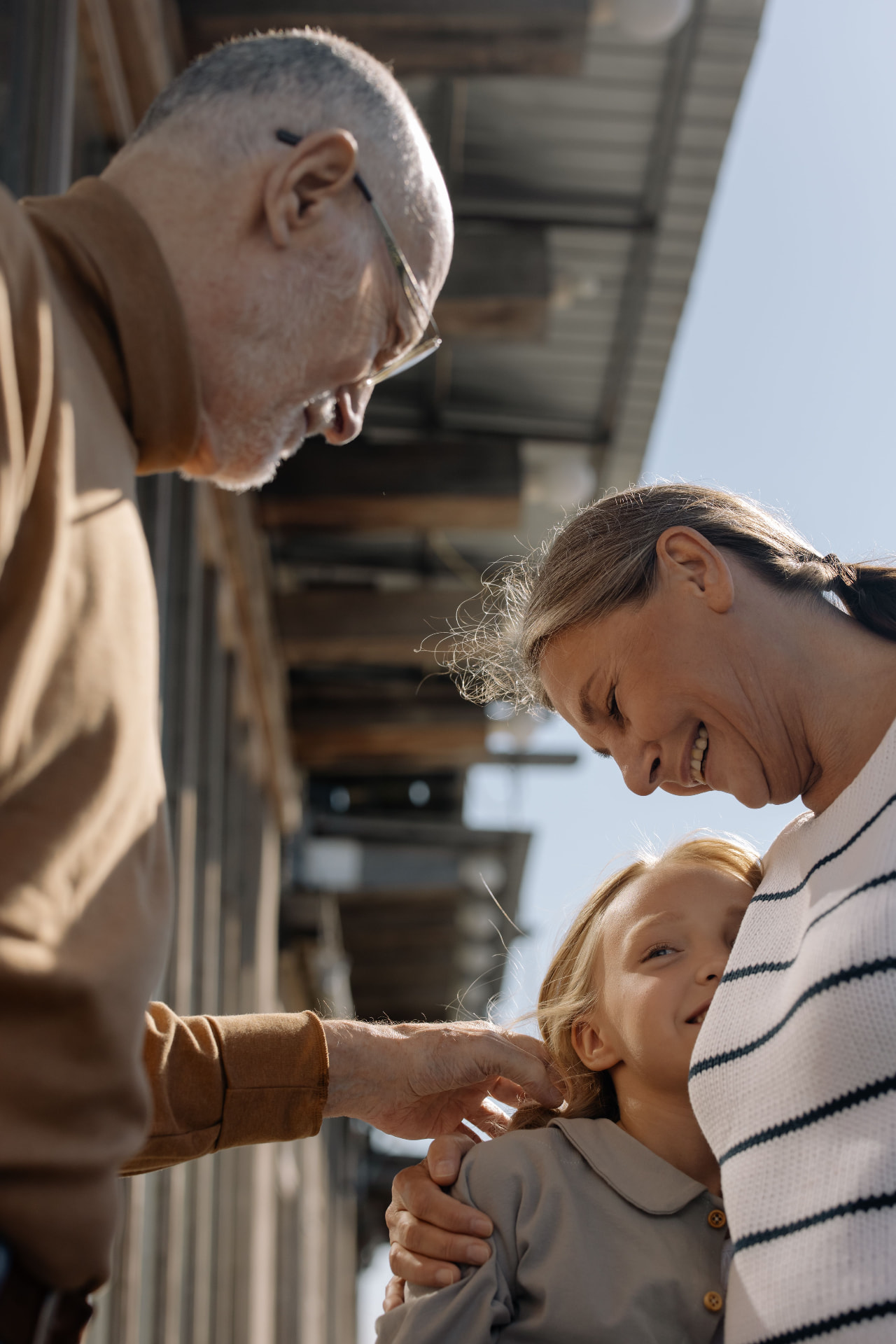 An older couple smiling warmly with their young granddaughter on a sunny porch