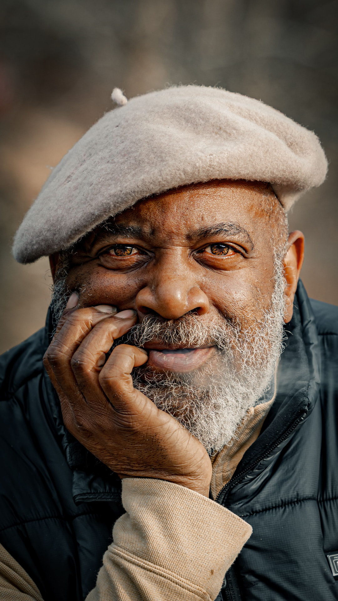 A smiling older man in a wool cap resting his chin on his hand